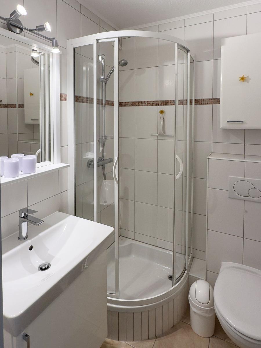 Badezimmer mit Dusche, Waschbecken und Toilette. Weiße Fliesen und Spiegelschrank.