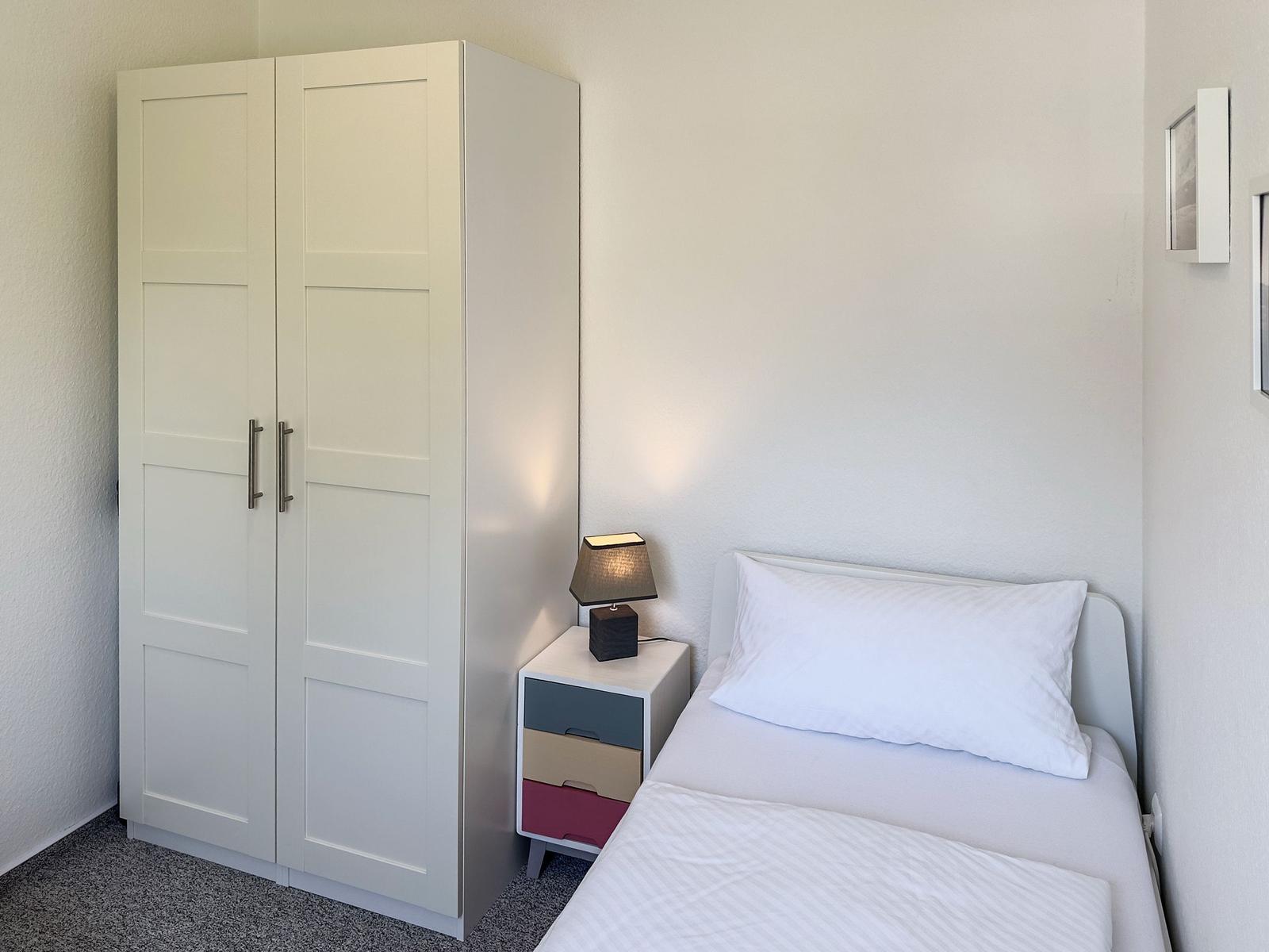 Ein Schlafzimmer mit einem Bett, einem Schrank und einem Nachttisch mit Lampe.