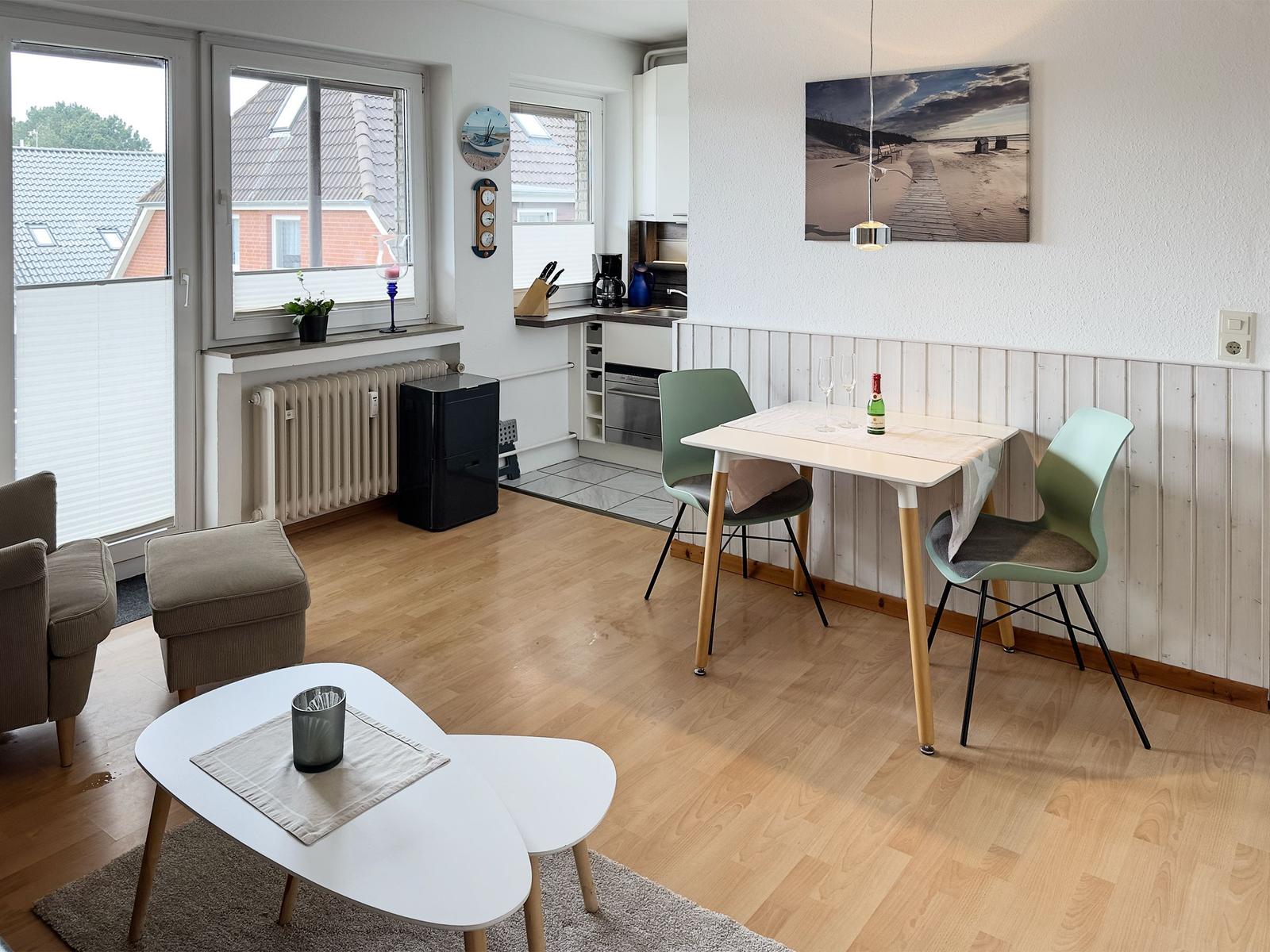 Living and dining area with table, chairs, and windows. Kitchen with worktop and appliances.