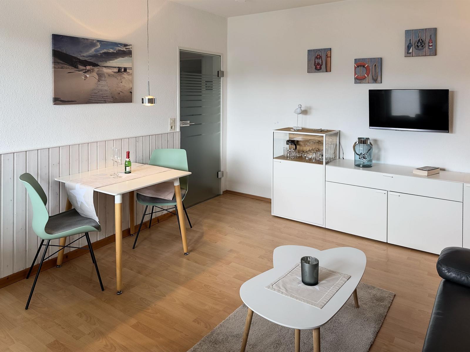 Living room with dining table, TV, and white cabinets. Wooden floor and wall picture.