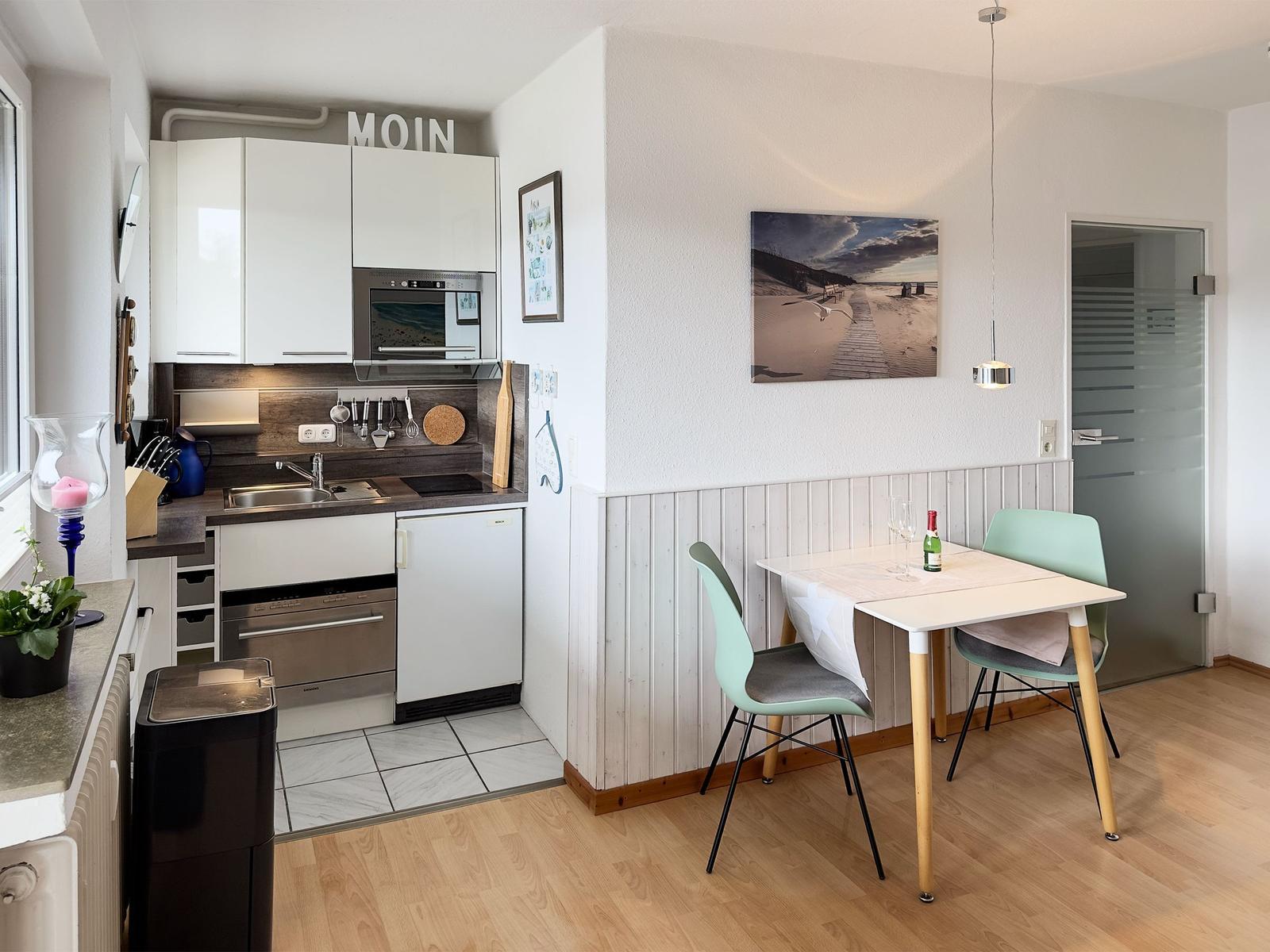 Kitchen with dining area, table with two chairs, wall picture and door