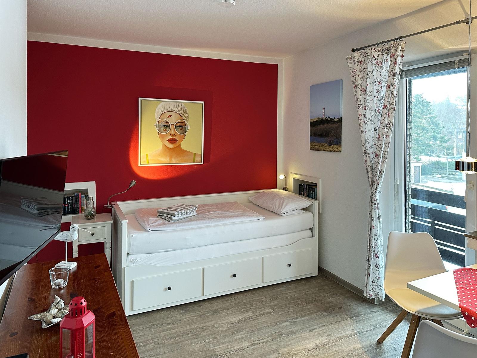 Schlafzimmer mit weißem Bett, roter Wand und Blick auf Balkon.