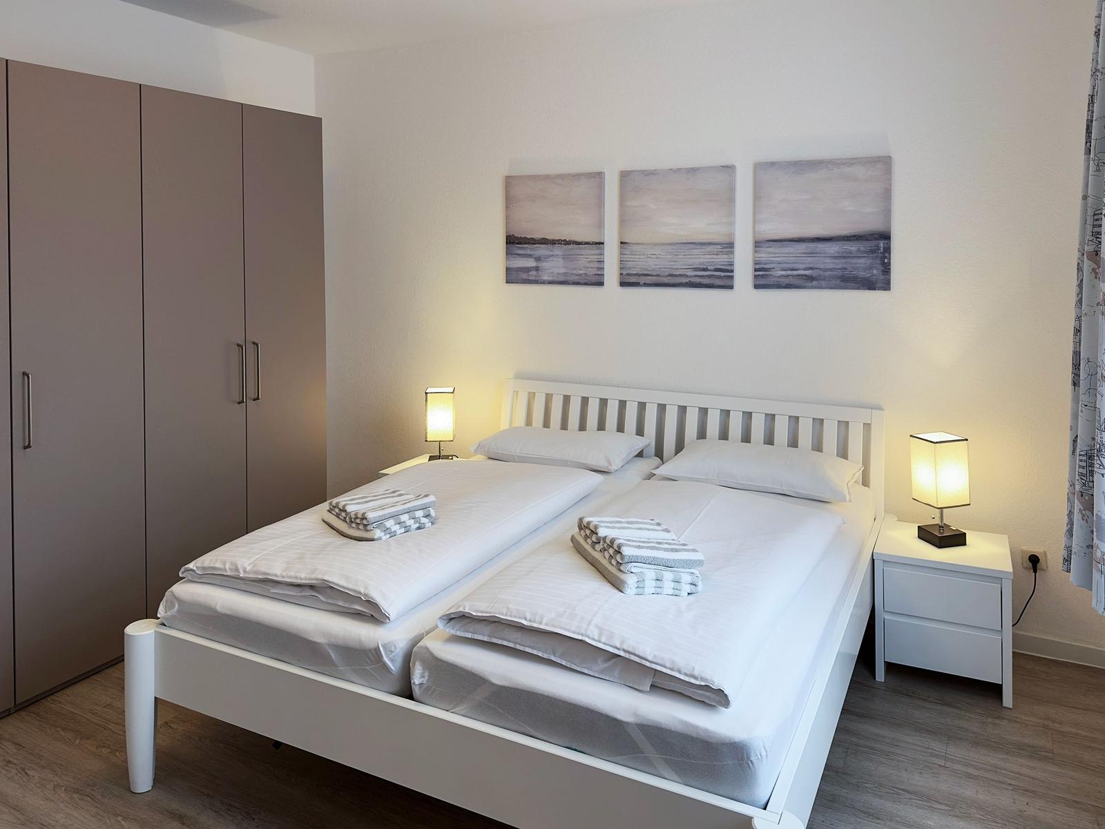 Zimmer mit Doppelbett, Nachttischen und Wandbildern.