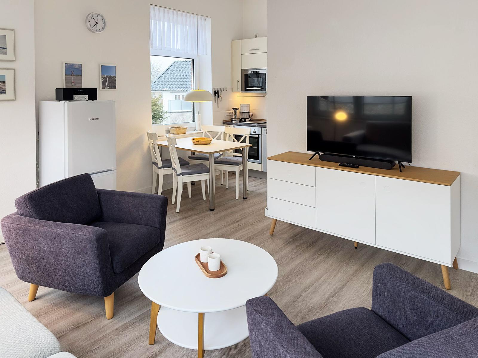 Wohnzimmer mit Essbereich, Küchenzeile und Fernseher auf Schrank