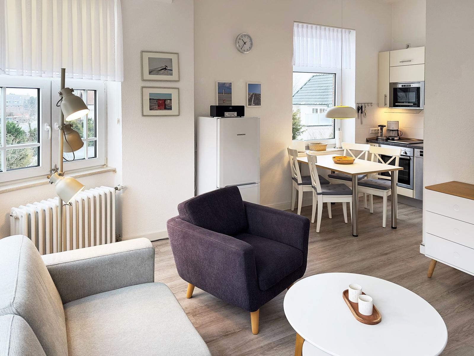 Wohnzimmer mit Essbereich und Küche. Ein dunkler Sessel und ein weißer Tisch sind sichtbar.