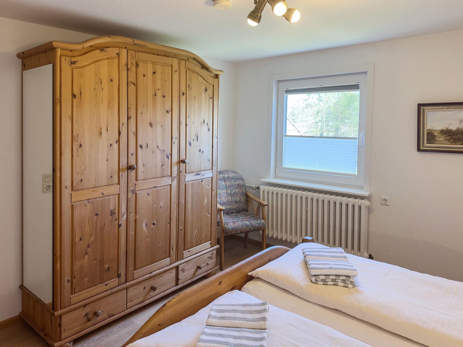 Schlafzimmer mit Holzschrank, Bett und Fenster. An der Wand hängt ein Bild.