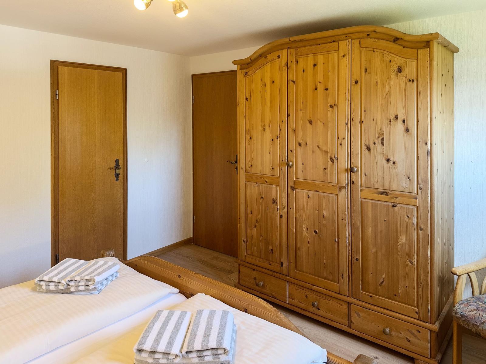 Schlafzimmer mit Holzbett, großer Kleiderschrank und gefalteten Handtüchern.