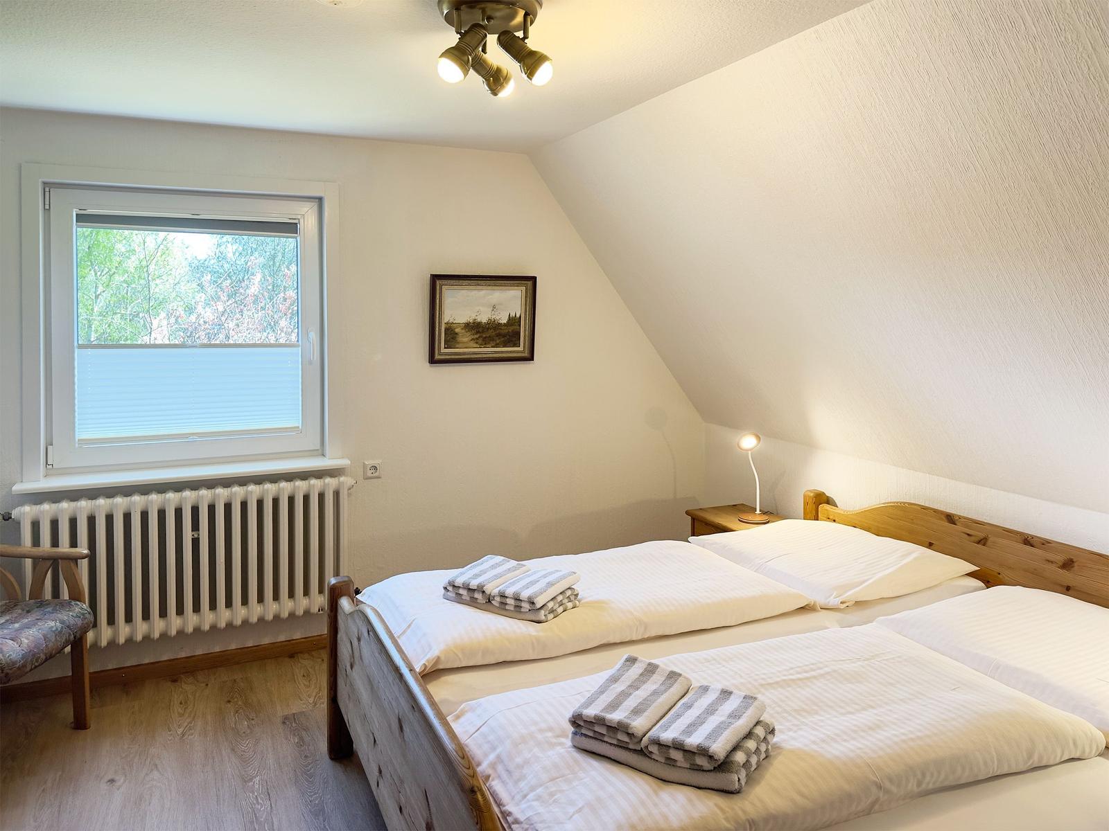 Schlafzimmer mit Doppelbett, Fenster und Holzboden.