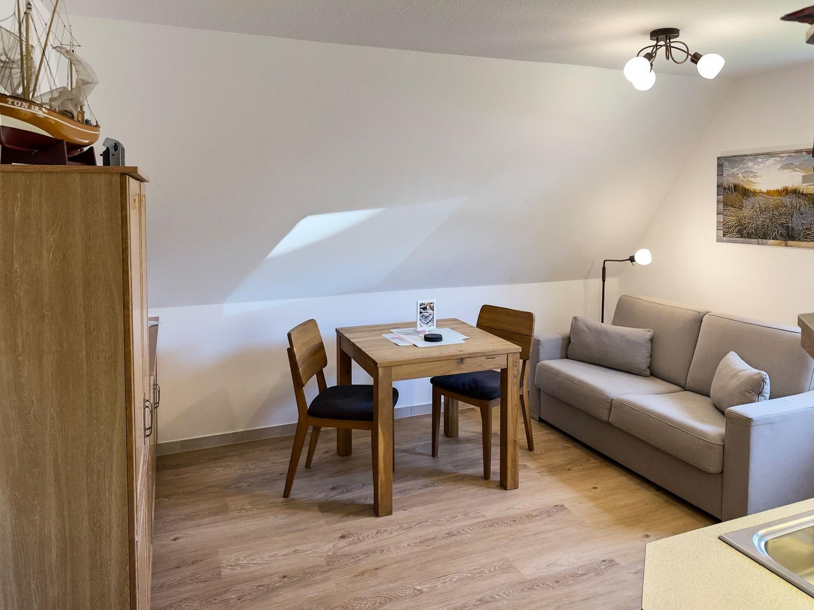 Wohnzimmer mit Sofa, Tisch und zwei Stühlen. Holzfußboden und Wandbild.