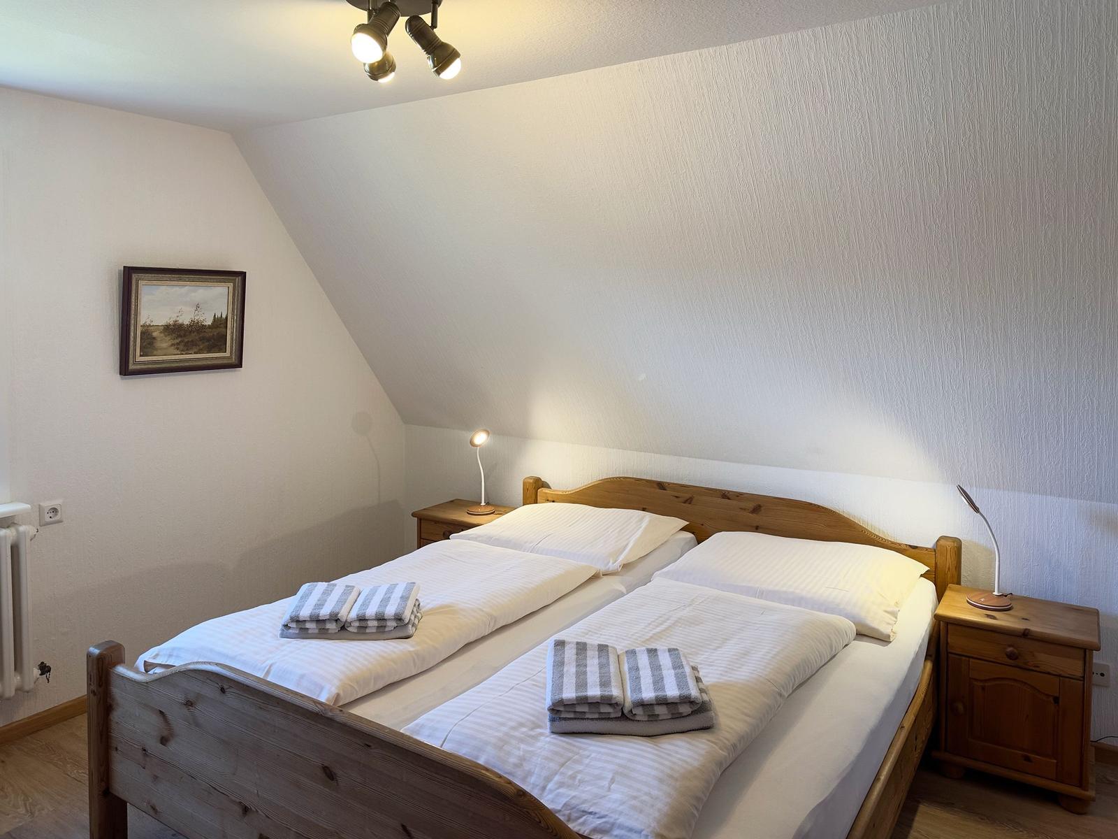 Doppelbett mit Holzrahmen, zwei Nachttische und Stehlampe in einem Schlafzimmer mit Dachschrägen.