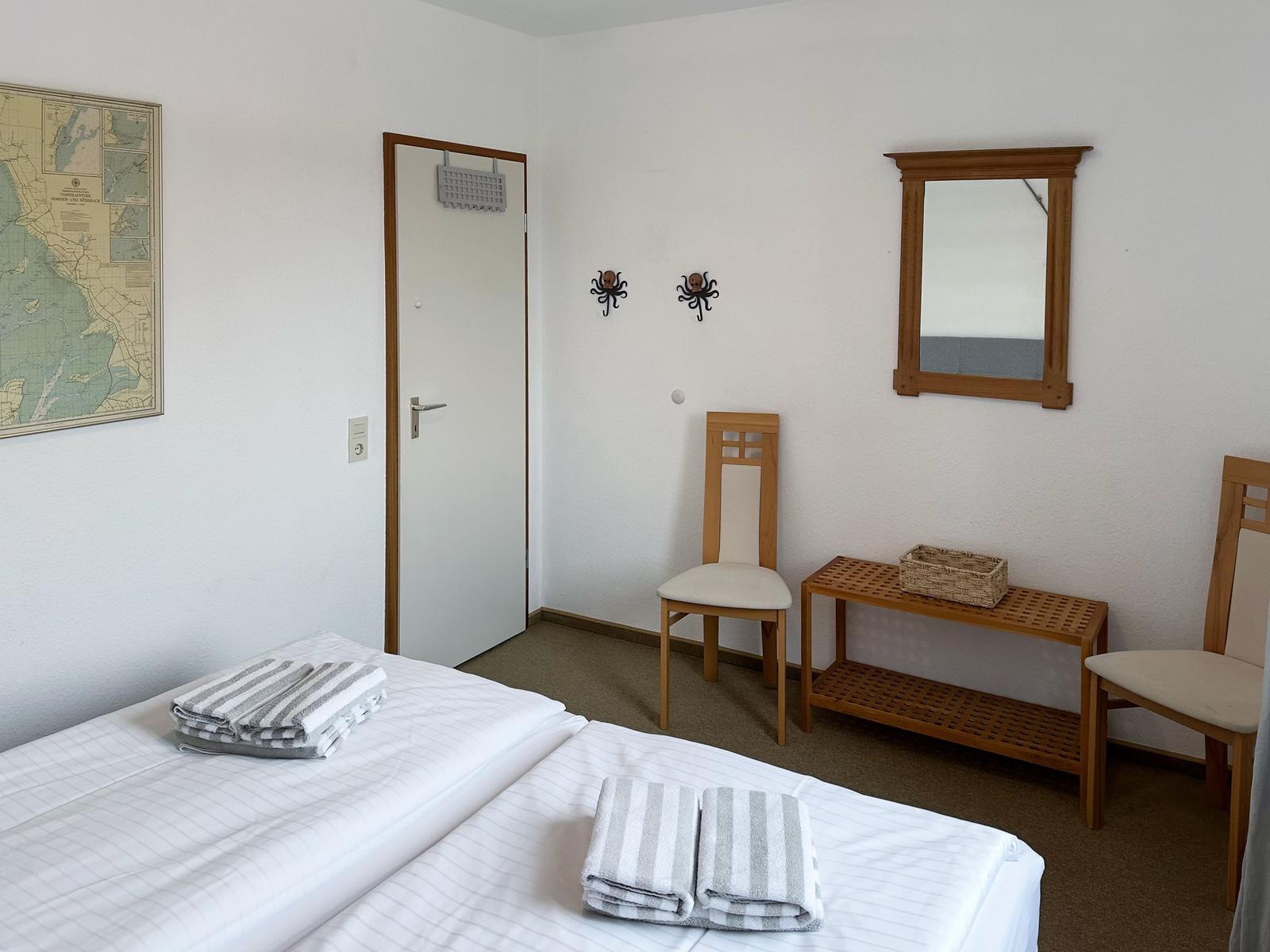 Room with two beds, wooden chairs, mirror, and map on wall.