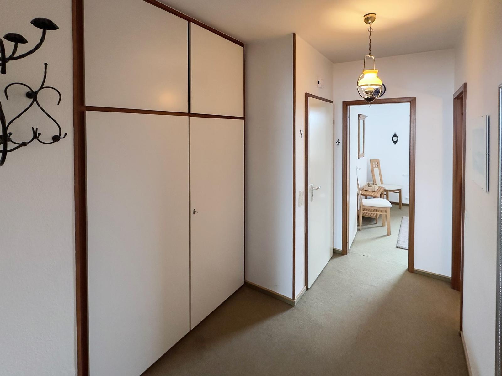Hallway with closet, door, and lamp. In the background, a dining area with chairs is visible.