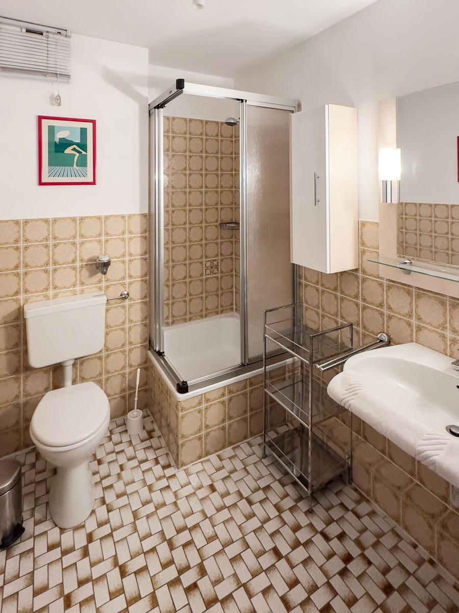 Bathroom with shower, sink and toilet. Tiles on walls and floor.