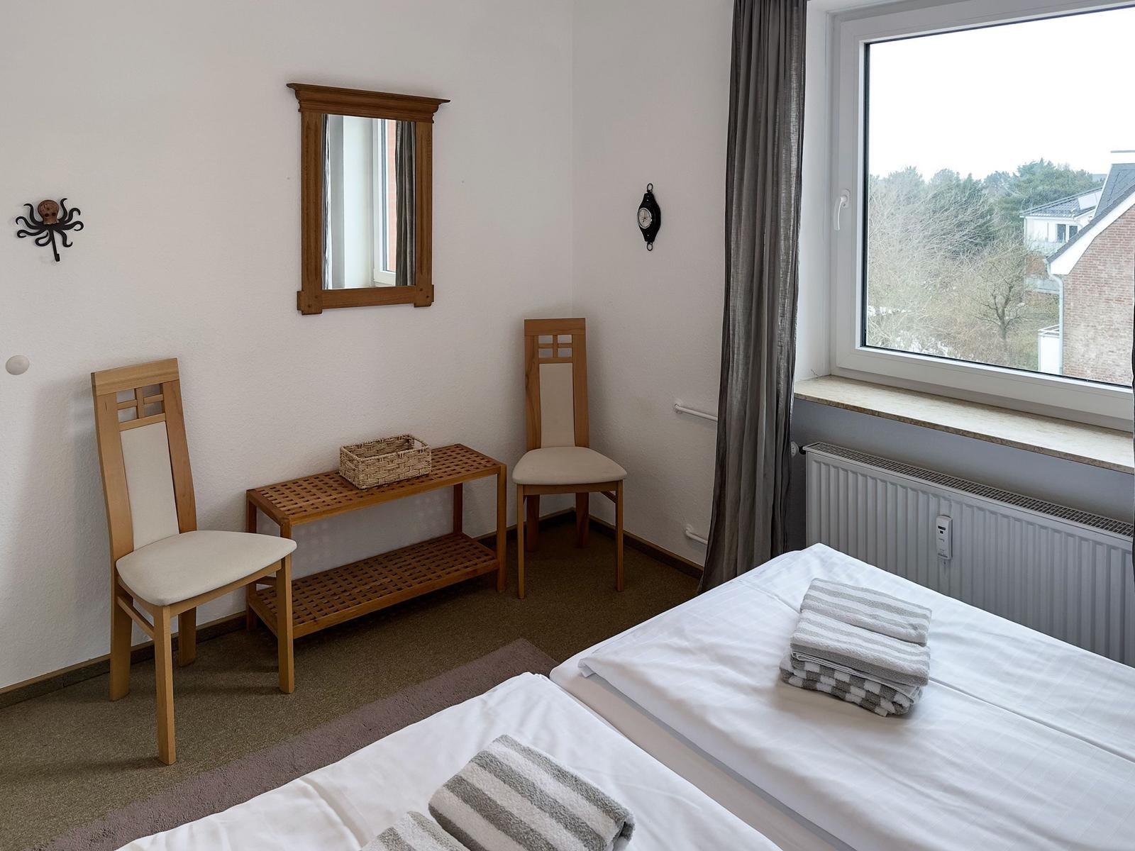 Room with two beds, mirror, chairs, and window with view.