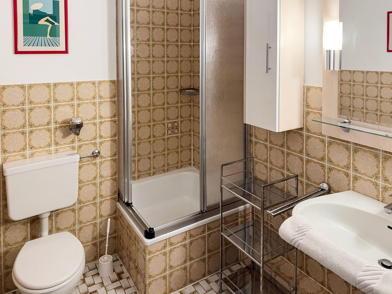 Bathroom with shower, sink, and toilet. Walls tiled with pattern.