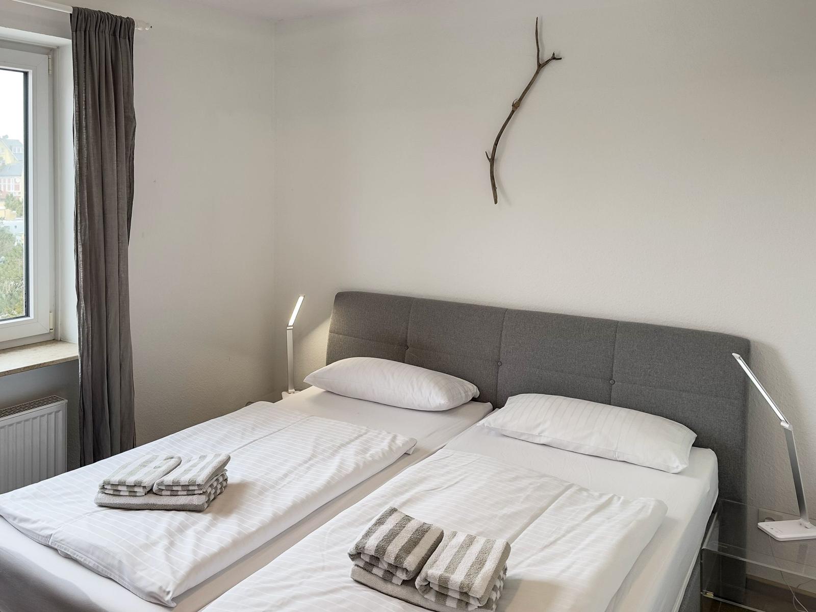 Room with double bed, window, nightstand, and wall decoration.