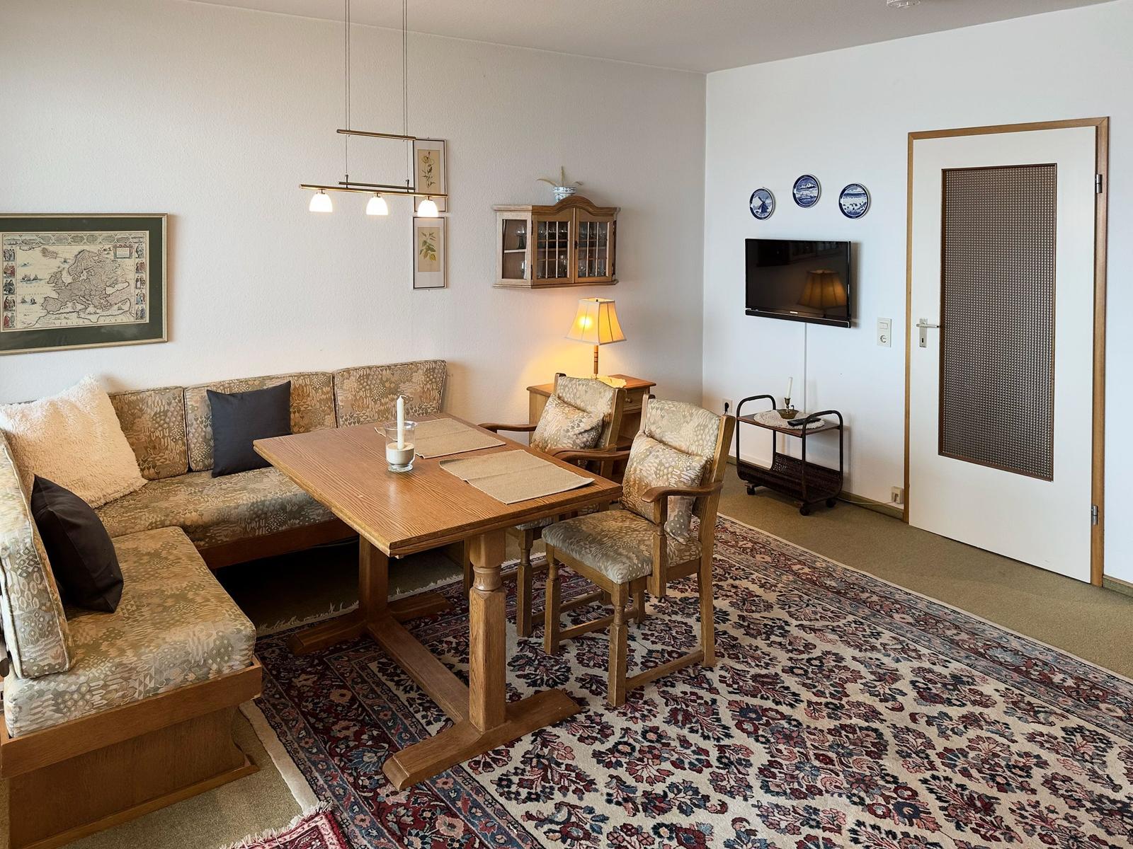 Living and dining area with wooden table, sofa, and TV mounted on the wall.