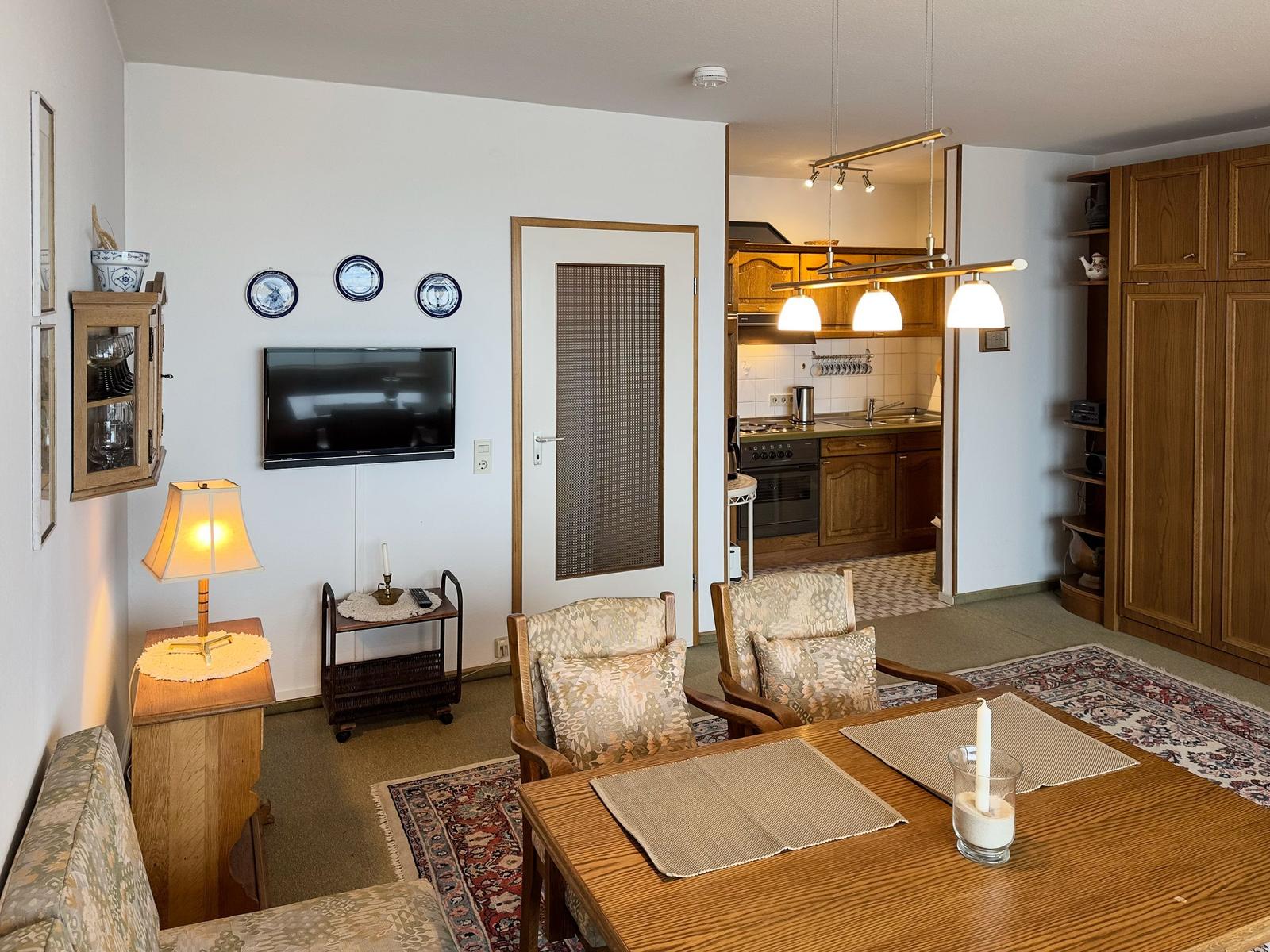 Living and dining area with kitchen. Wooden furniture, TV, and carpeted floor.