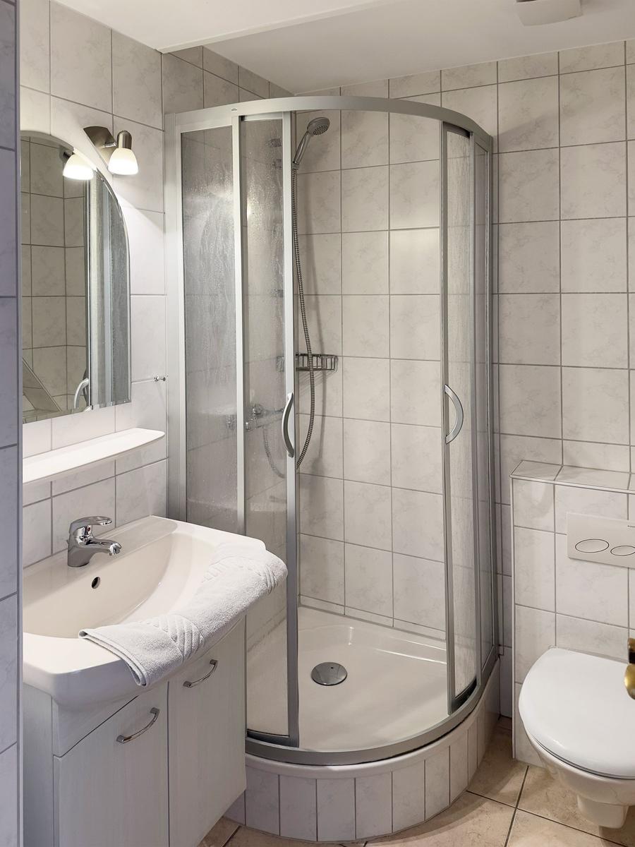 Badezimmer mit Duschkabine, Waschbecken und Toilette. Fliesenwand und Spiegel.