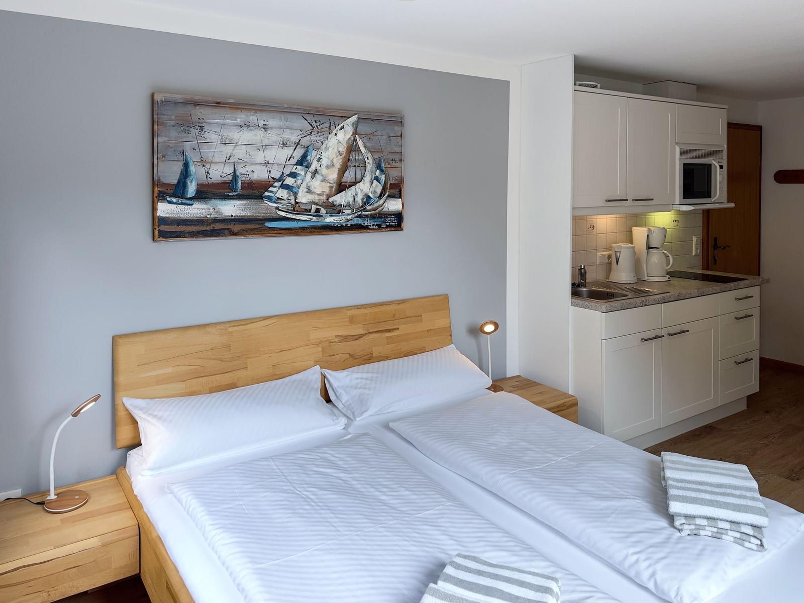 Schlafzimmer mit Doppelbett, Küchenzeile und Wandbild mit Segelbooten.