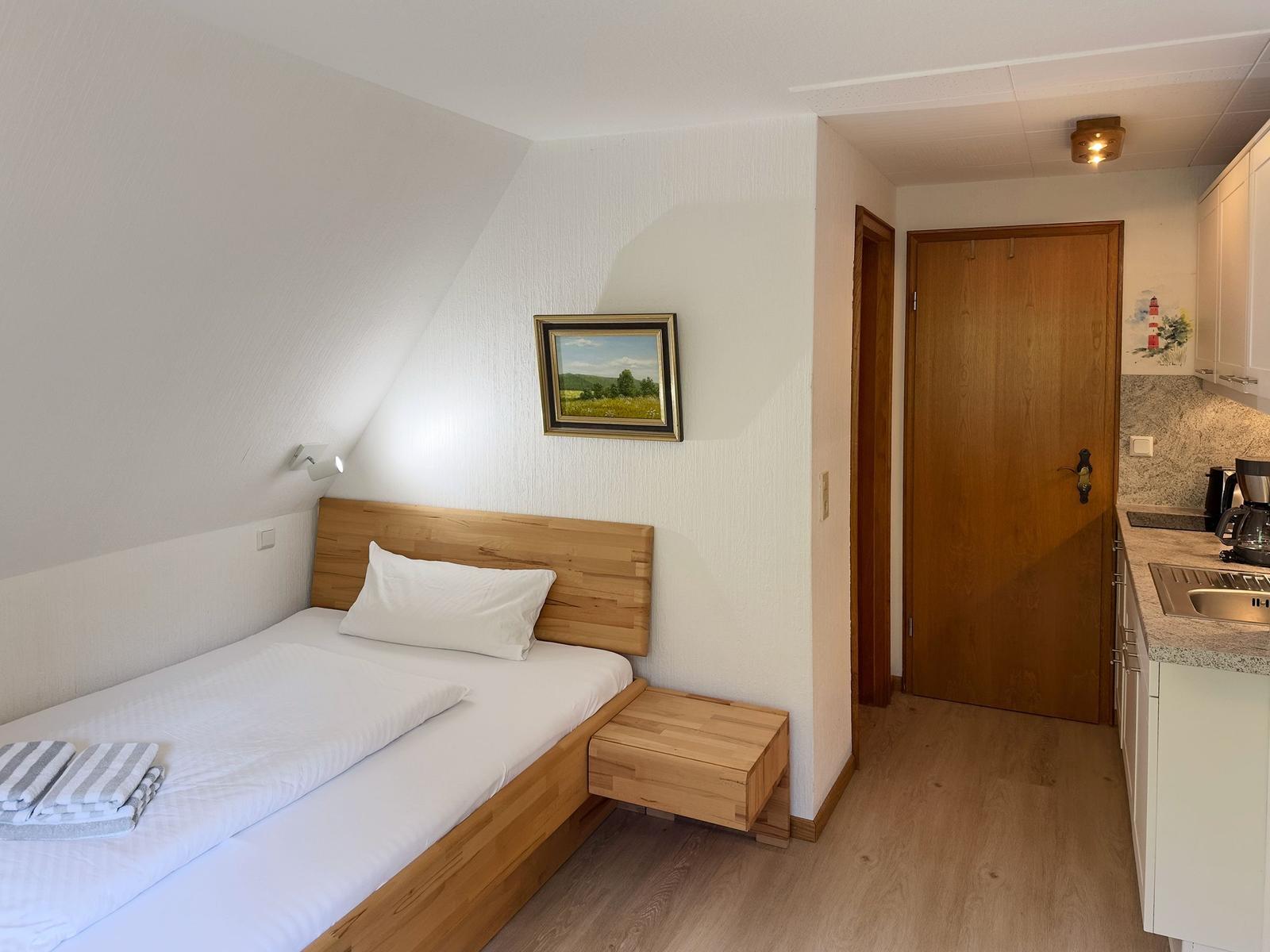 Schlafzimmer mit Bett, Nachttisch und Bild an der Wand. Küche mit Arbeitsplatte und Spüle.