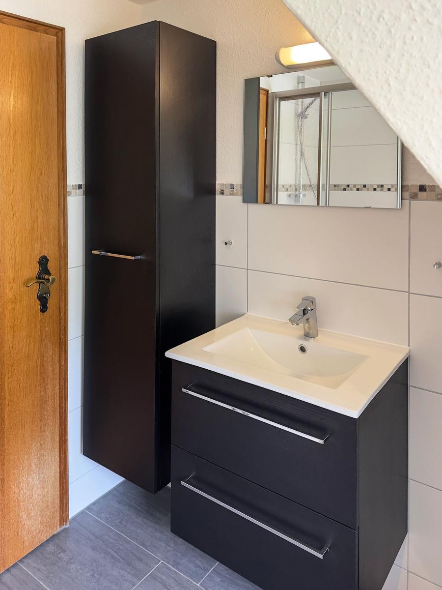 Badezimmer mit Waschbecken, Spiegelschrank und Duschbereich unter Dachschräge.