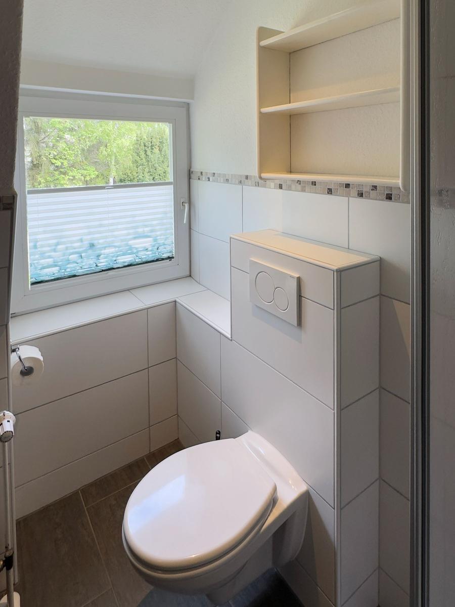 Badezimmer mit Toilette, Fenster und eingebautem Regal.