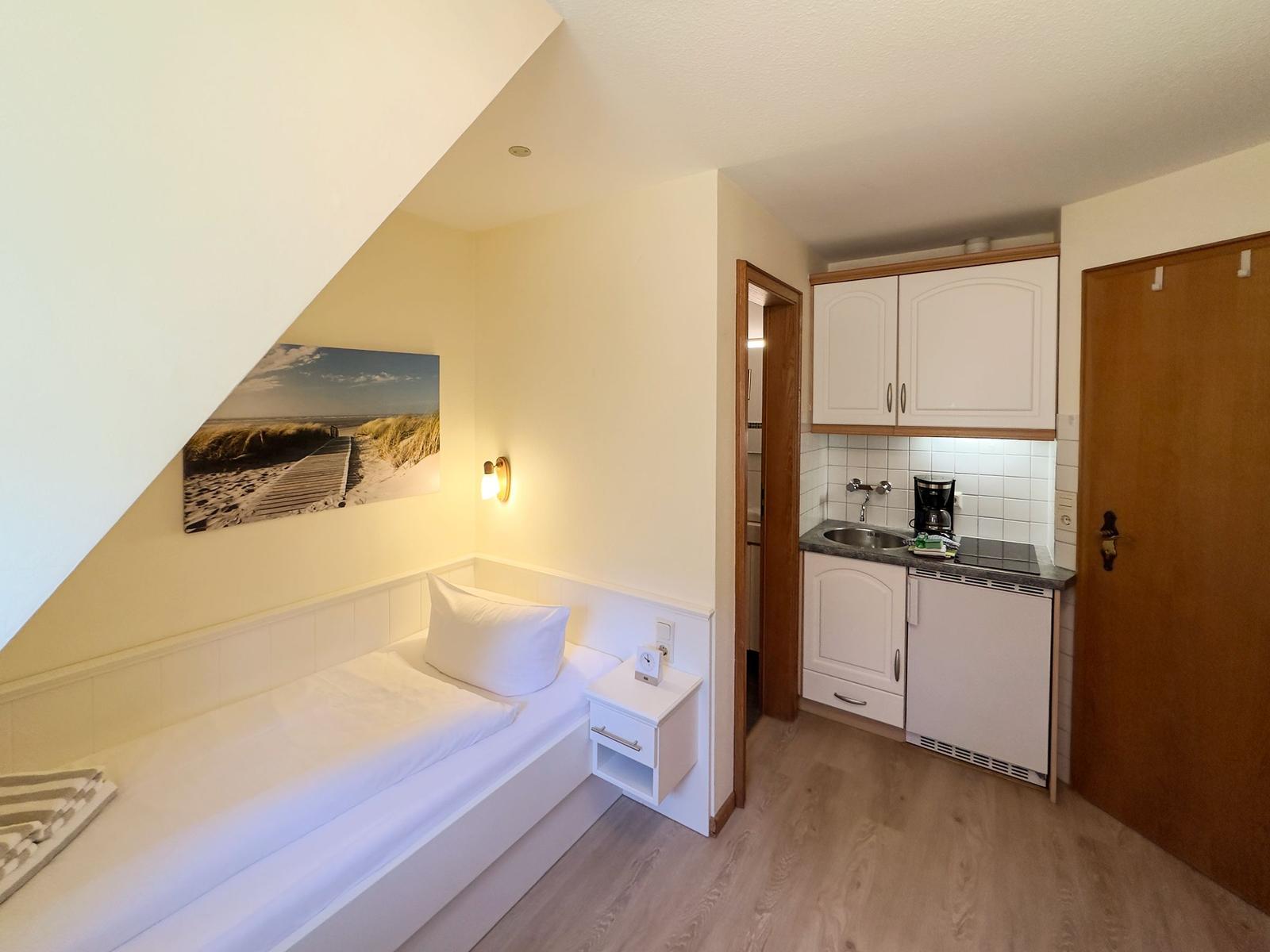 Schlafzimmer mit Bett, Nachttisch und Küchenbereich mit Spüle und Kühlschrank.