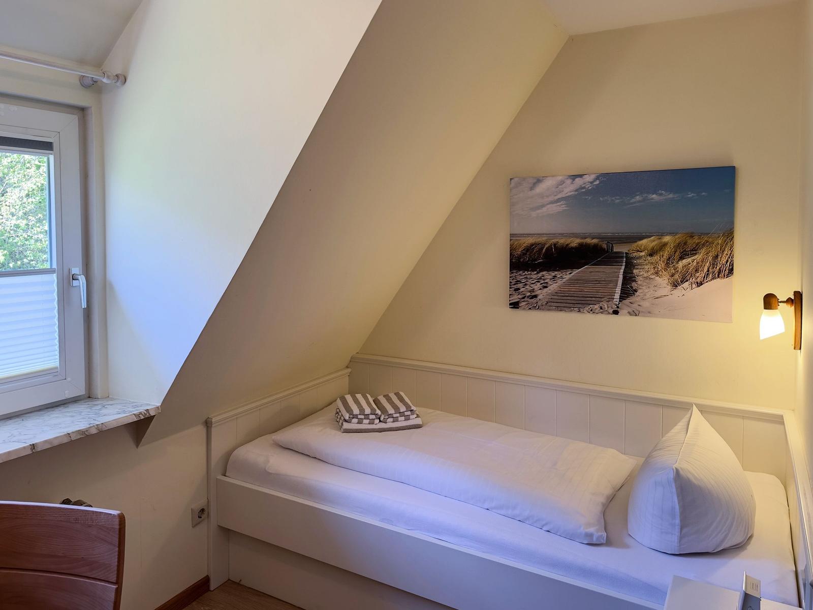 Ein Schlafzimmer mit Dachschrägen, Bett, Fenster und Wandbild.