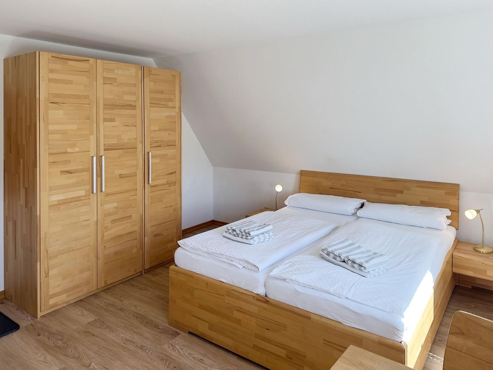 Schlafzimmer mit Holzbett und Kleiderschrank. Zwei Nachttische mit Lampen.