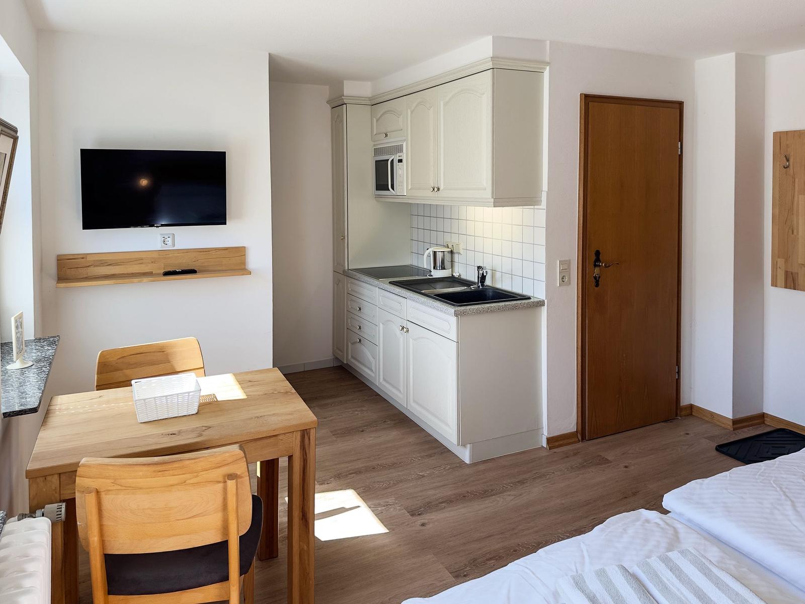 Küche mit Spüle, Mikrowelle und Arbeitsplatte. Essbereich mit Tisch und Stühlen. Fernseher an der Wand.