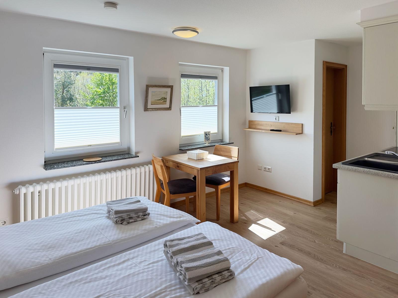 Zwei Betten, Tisch mit Stühlen, TV und Fenster mit Blick auf Wald.