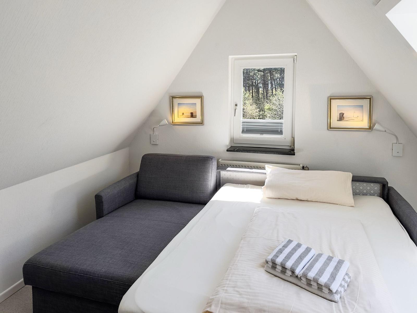 Ein Schlafzimmer mit Dachschräge, Bett und Fenster mit Blick auf Wald.