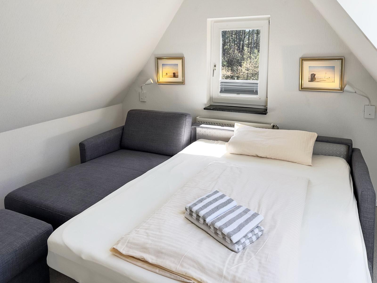 Schlafzimmer mit Bett, Sofa und Fenster mit Blick auf Wald.