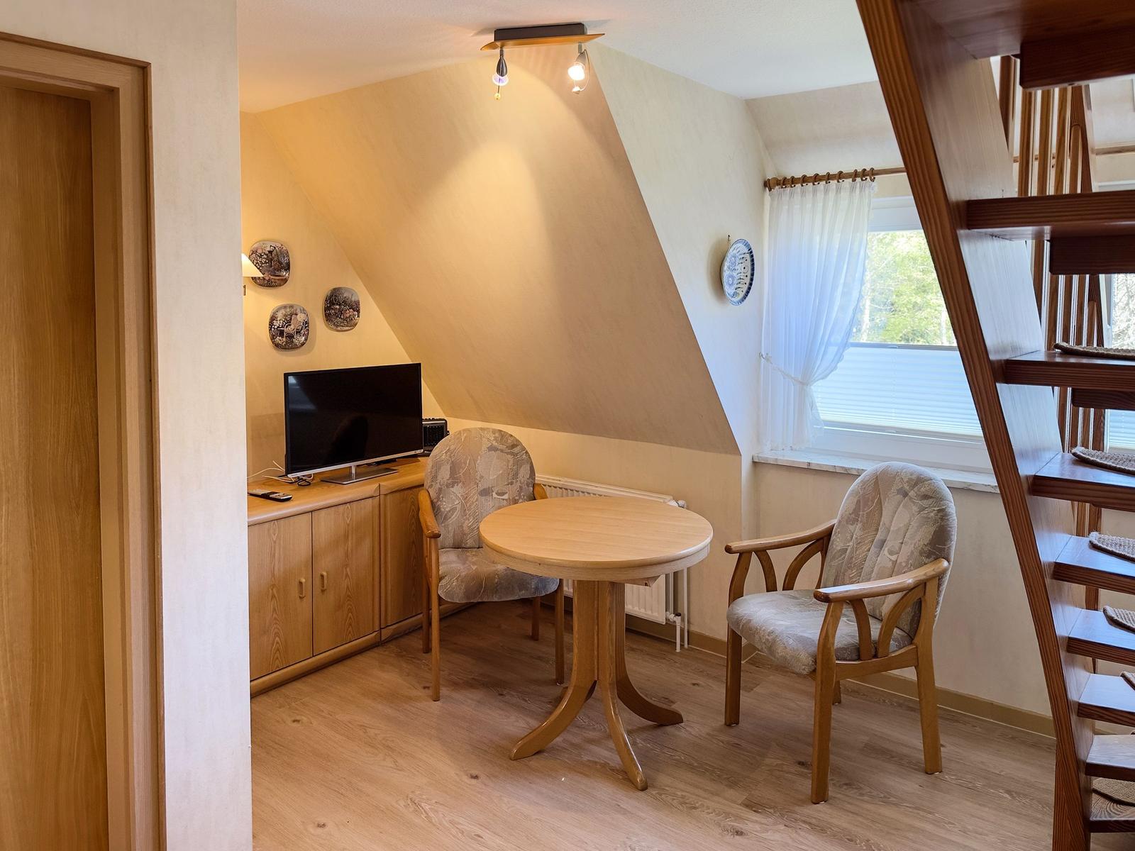 Ein Raum mit Tisch, zwei Stühlen, Fernseher und Fenster mit Blick nach draußen.