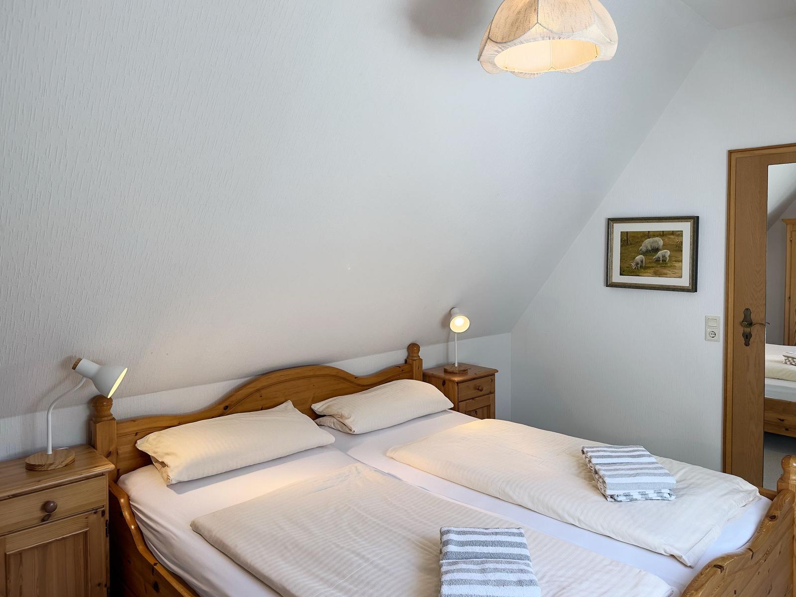 Schlafzimmer mit Doppelbett, Holzmöbel und Stehlampe. Decke geneigt, Wandbild mit Schafen.