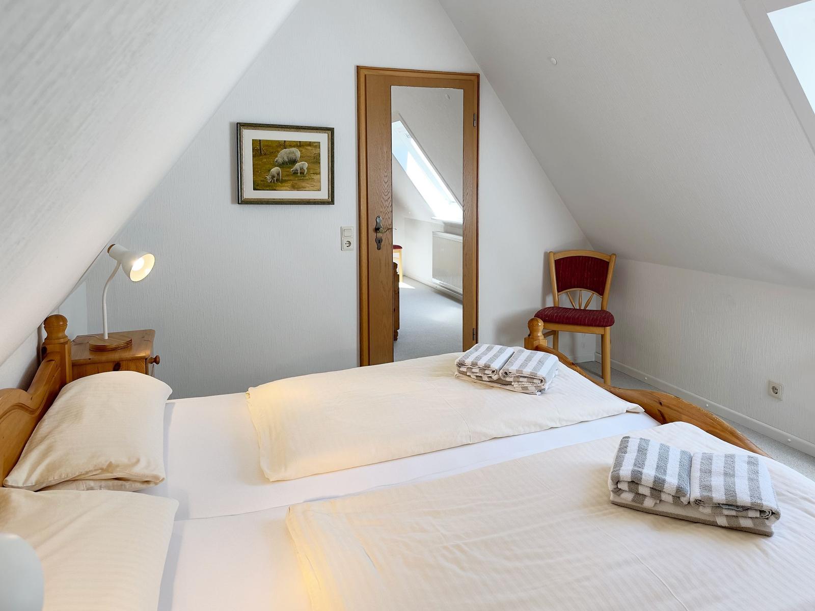 Schlafzimmer mit Dachschrägen, Bett, Stuhl und Bild an der Wand.