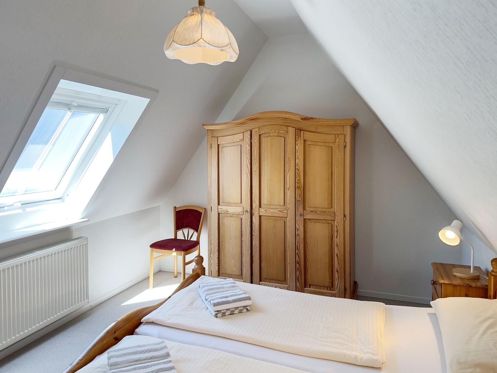 Schlafzimmer mit Dachschrägen, Bett, Kleiderschrank, Stuhl und Dachfenster.