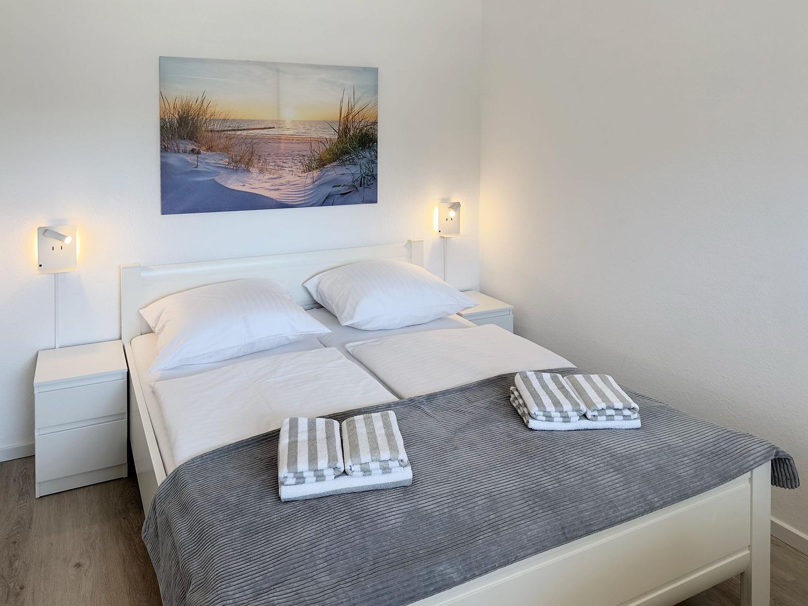 Bedroom with double bed, two nightstands, and wall art. Towels on bed.