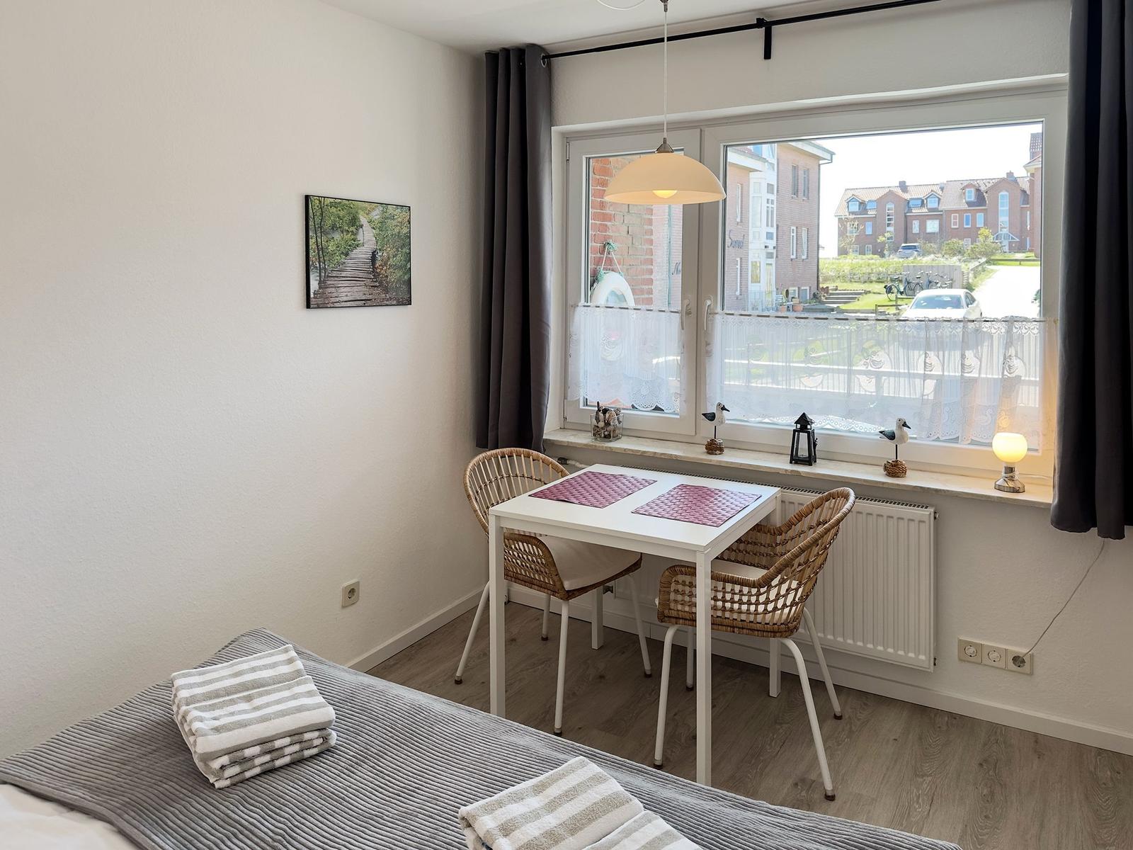 Room with table, two chairs, and bed. Window with view of residential area.