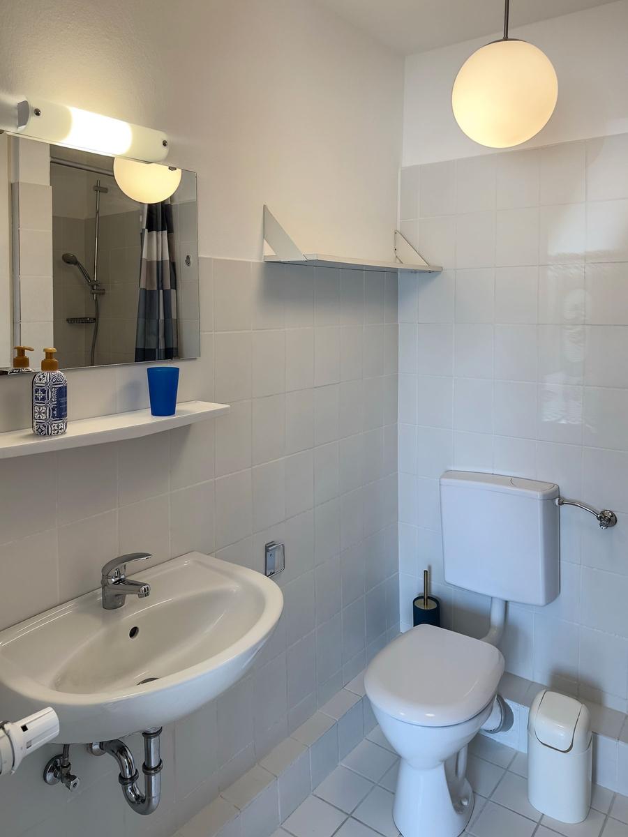 Bathroom with sink, toilet, and mirror. White tiles and modern lighting.