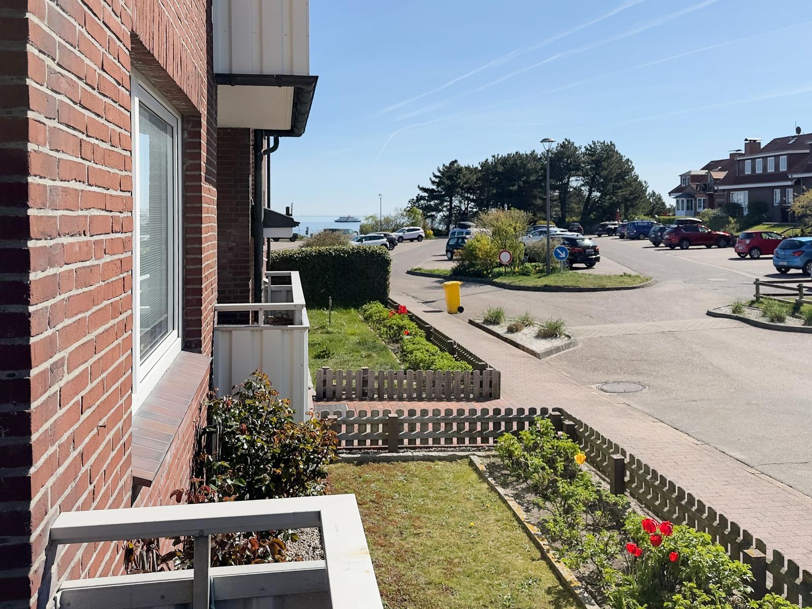 Red brick house with balcony, view of parking lot and green areas.