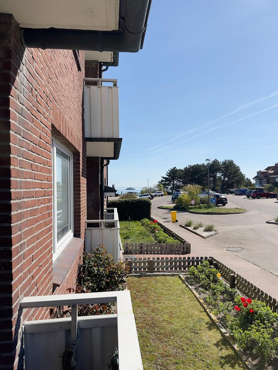 View from balcony onto street with parking lot and trees under blue sky.