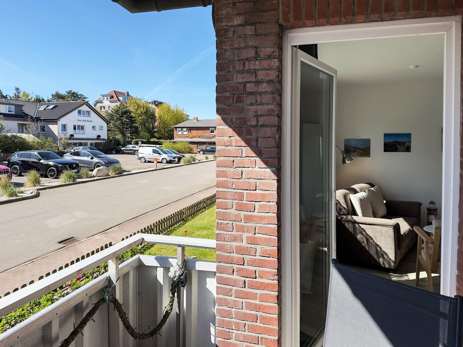 Terrace with view of street and parking lot. Entrance to living room with sofa and wall pictures.