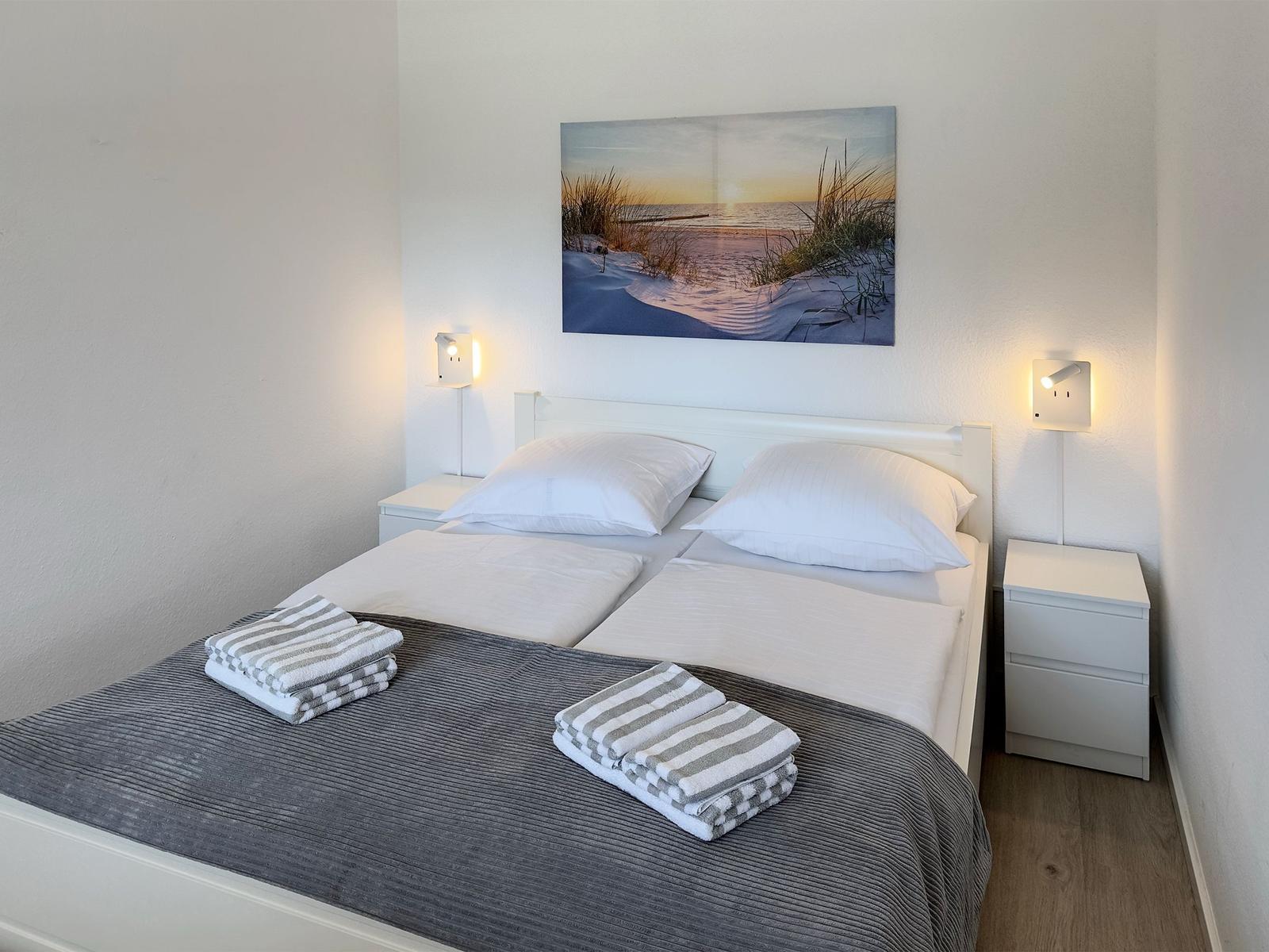 Bedroom with bed, two nightstands, and wall art. Towels are on the bed.