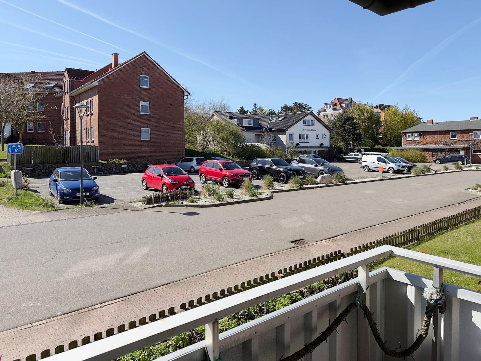 View of parking lot with cars and surrounding houses under blue sky.