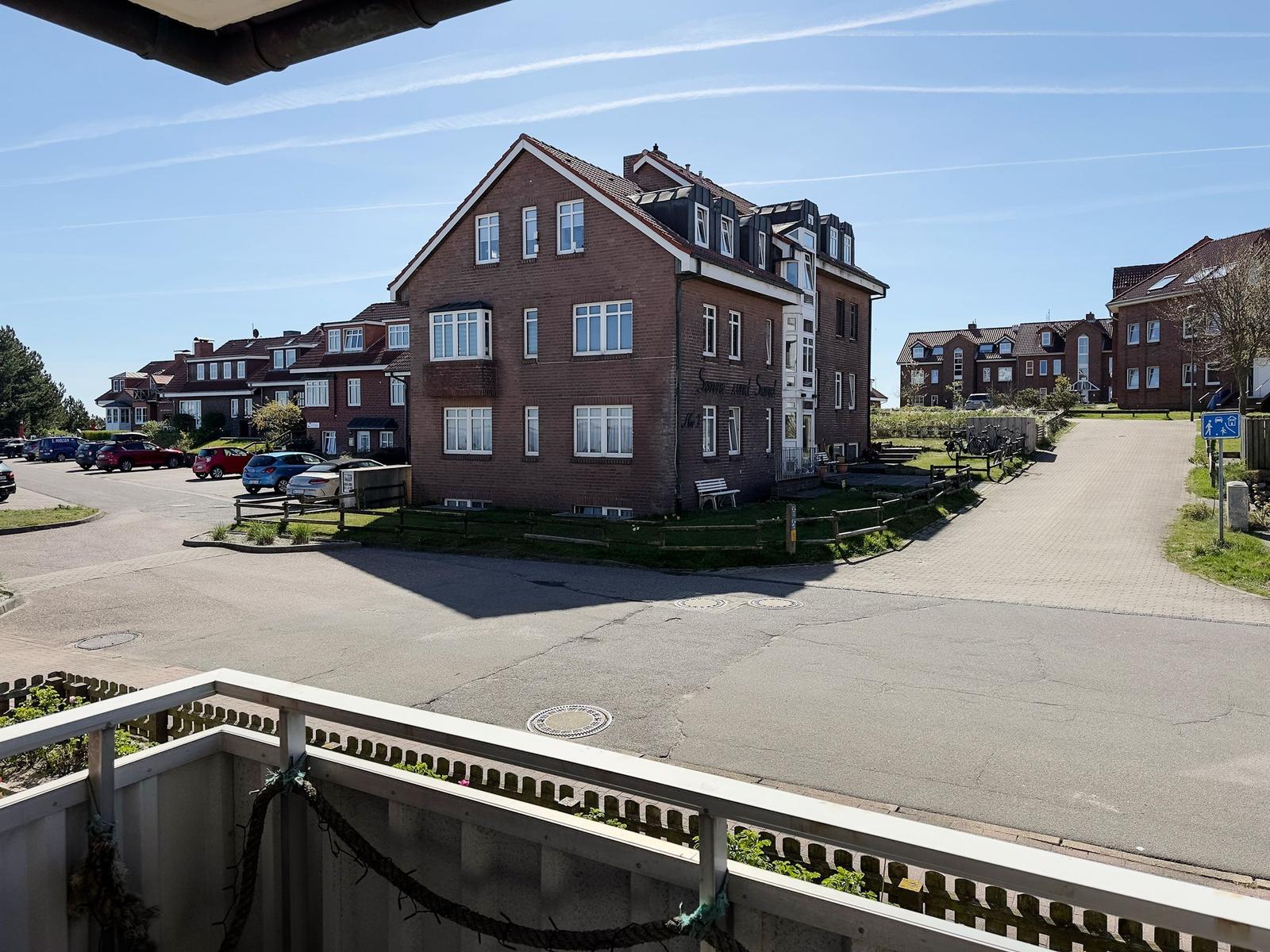 Villa with balcony, parking lot, and adjacent houses under blue sky.
