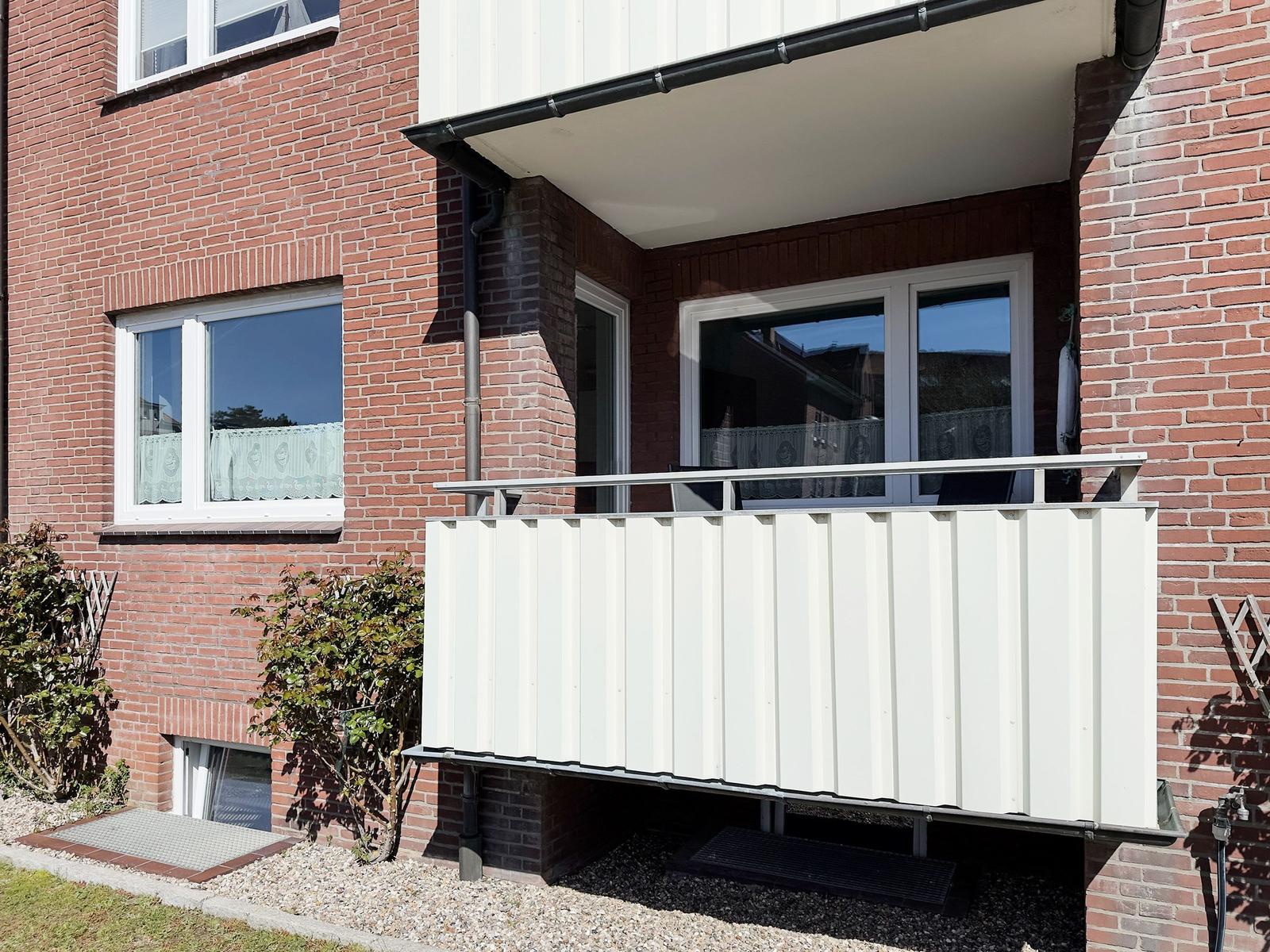 Single-family house with balcony, red brick, and white windows.