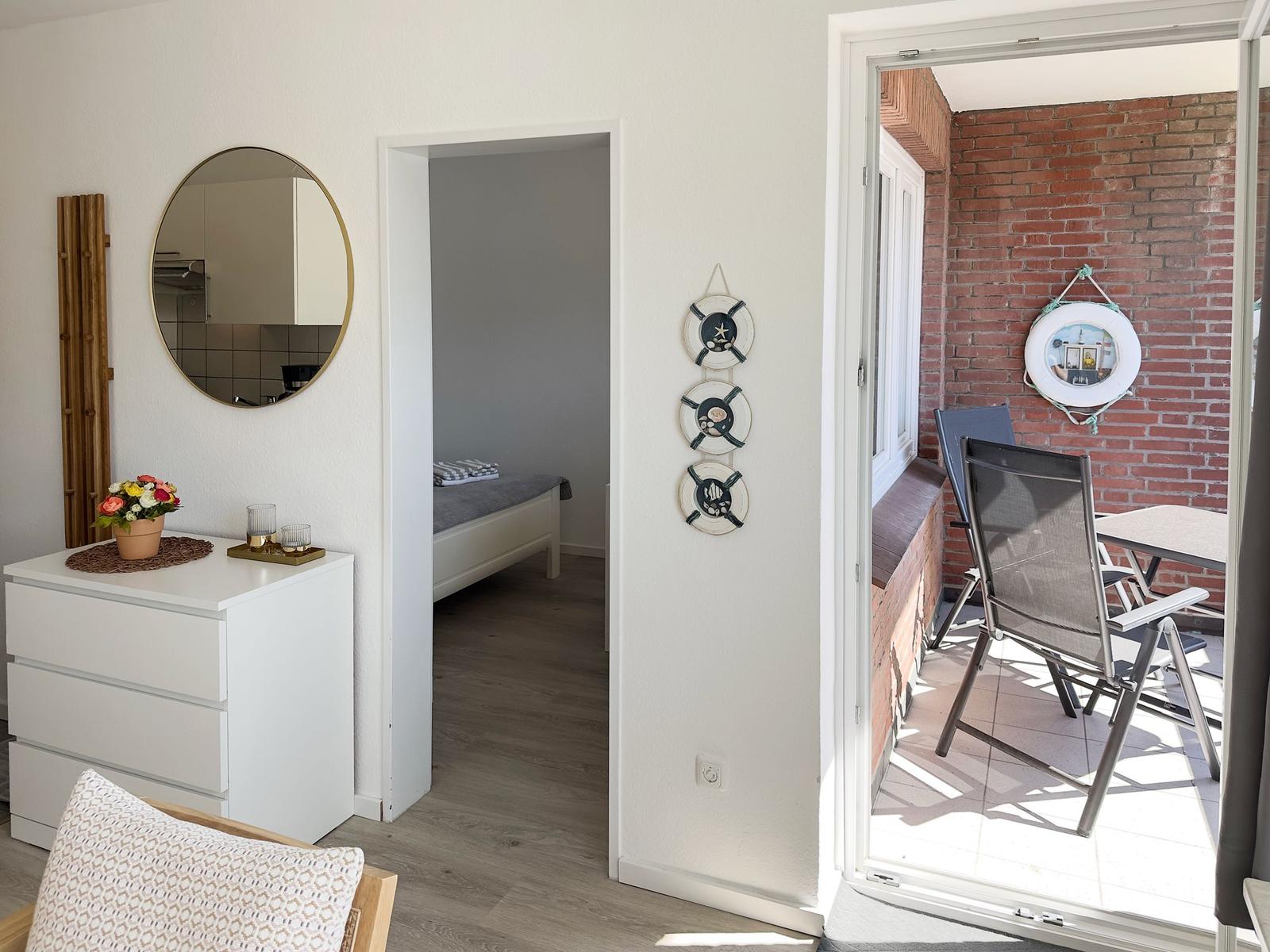 Living area with bedroom and balcony. Round mirrors and wooden furniture.