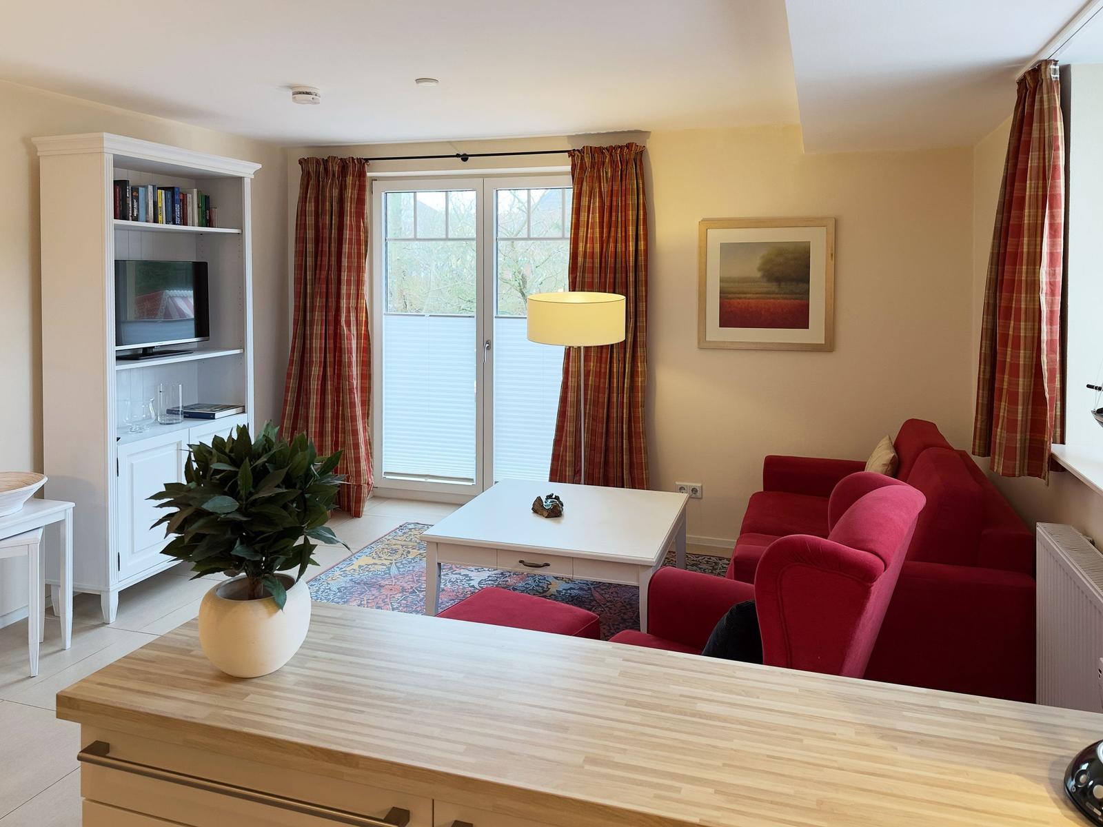 Wohnzimmer mit rotem Sofa, weißen Möbeln und Plaidvorhängen.